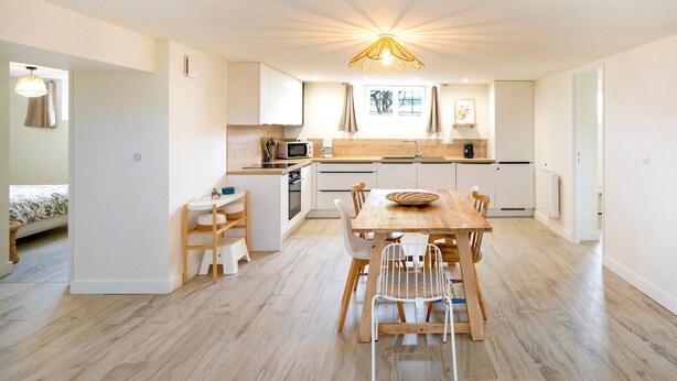 Una cocina moderna con armarios de madera, una mesa de comedor con sillas y una lámpara colgante.