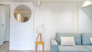 Una sala de estar moderna con un sofá azul claro, un espejo redondo y un taburete de madera.