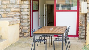 Un muro de piedra, una mesa de madera con sillas y una puerta con marco rojo.