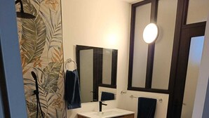 Un baño con tocador de madera, espejo, lavamanos y ducha con diseño de papel tapiz floral.