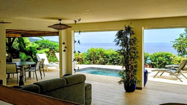 Una sala de estar moderna con piscina, mobiliario exterior y vista al océano.