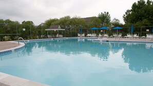 Une piscine à l’eau d’un bleu cristallin, entourée de chaises longues blanches et de parasols bleus.