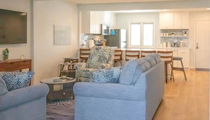 A living room with a sofa, armchairs, a coffee table, and a TV. There is a kitchen in the background with cabinets and a window. - Charming Bethany Beach Getaway Pickle Ball (Bethany Beach)