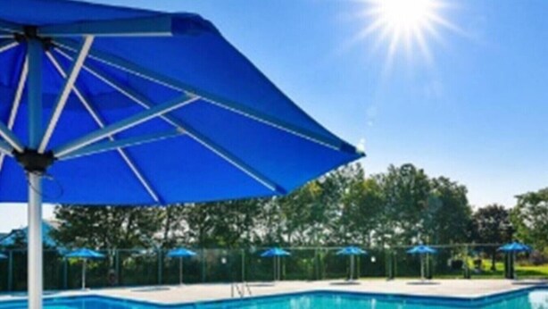 Une piscine avec un parasol bleu et un ciel d’un bleu limpide.