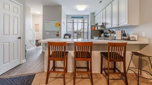Une cuisine moderne avec des meubles blancs, un îlot central doté de tabourets de bar et une enseigne visible au-dessus de l’îlot.