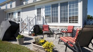 Une terrasse couverte, aménagée avec du mobilier d’extérieur, un barbecue et des plantes en pot.