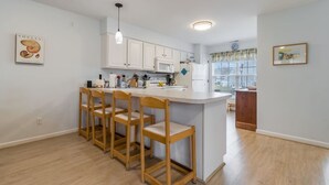 Une cuisine moderne avec des meubles blancs, un îlot central doté de tabourets et un luminaire suspendu.