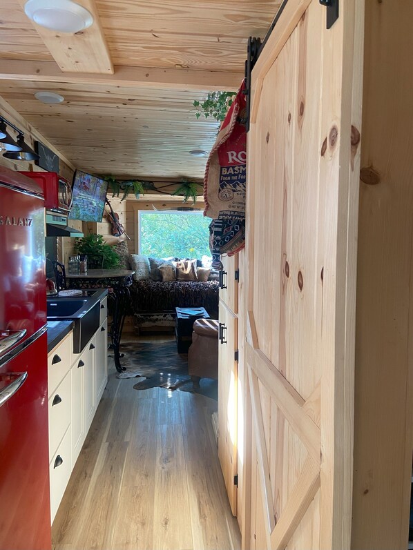 Cocina de madera estrecha con un refrigerador rojo, estufa y pileta. Se ve un ventanal con vista a la vegetación.