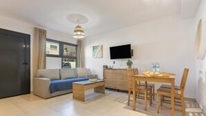Un soggiorno moderno con divano, tavolino, tavolo da pranzo, sedie, televisore e mobile contenitore.