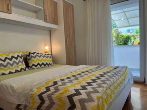 Une chambre à coucher comprenant un lit, une table de chevet, une lampe fixée au mur et une porte-fenêtre coulissante donnant sur l’extérieur.