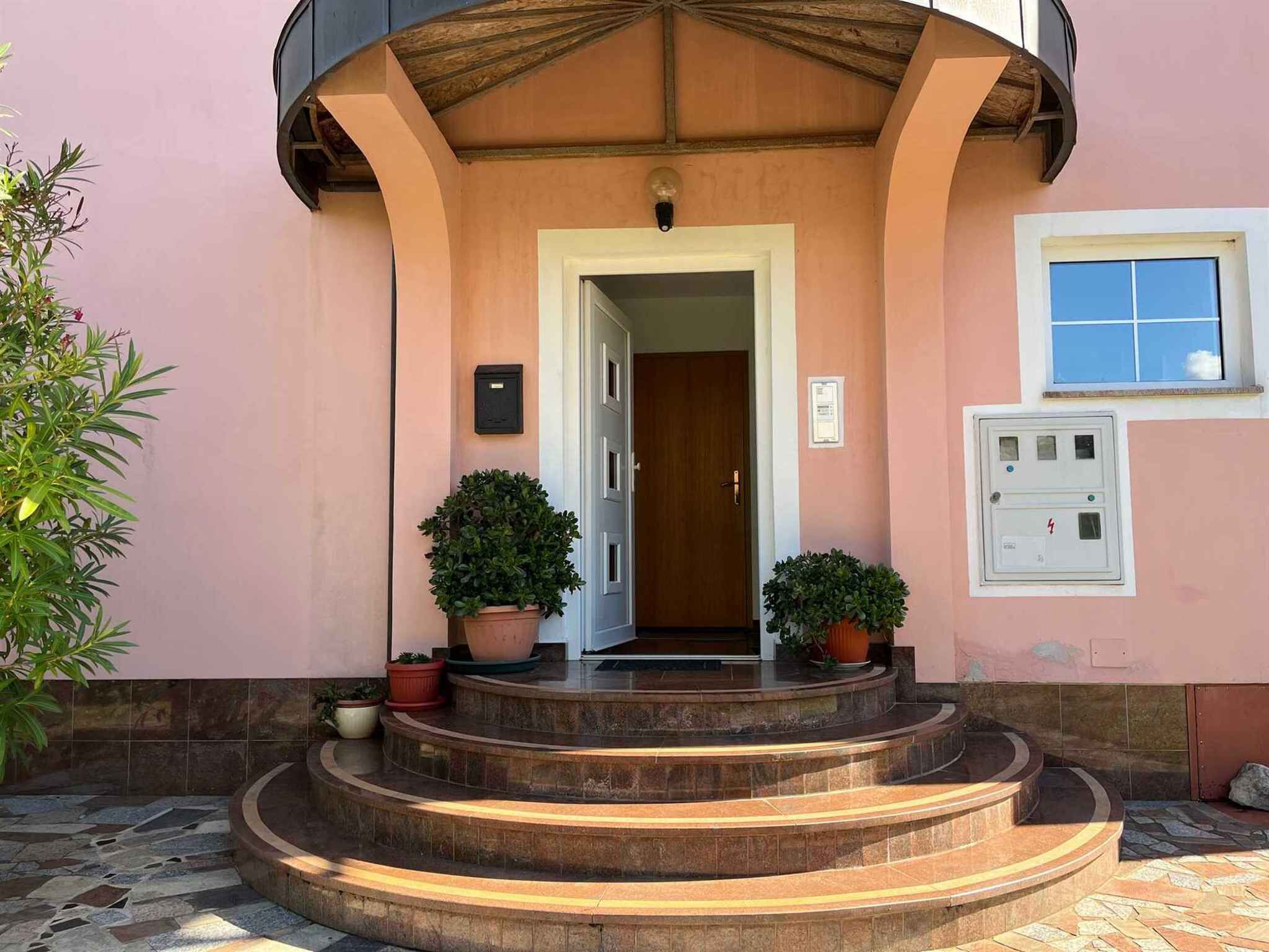A building entrance with a wooden door, potted plants, and a tiled floor.
