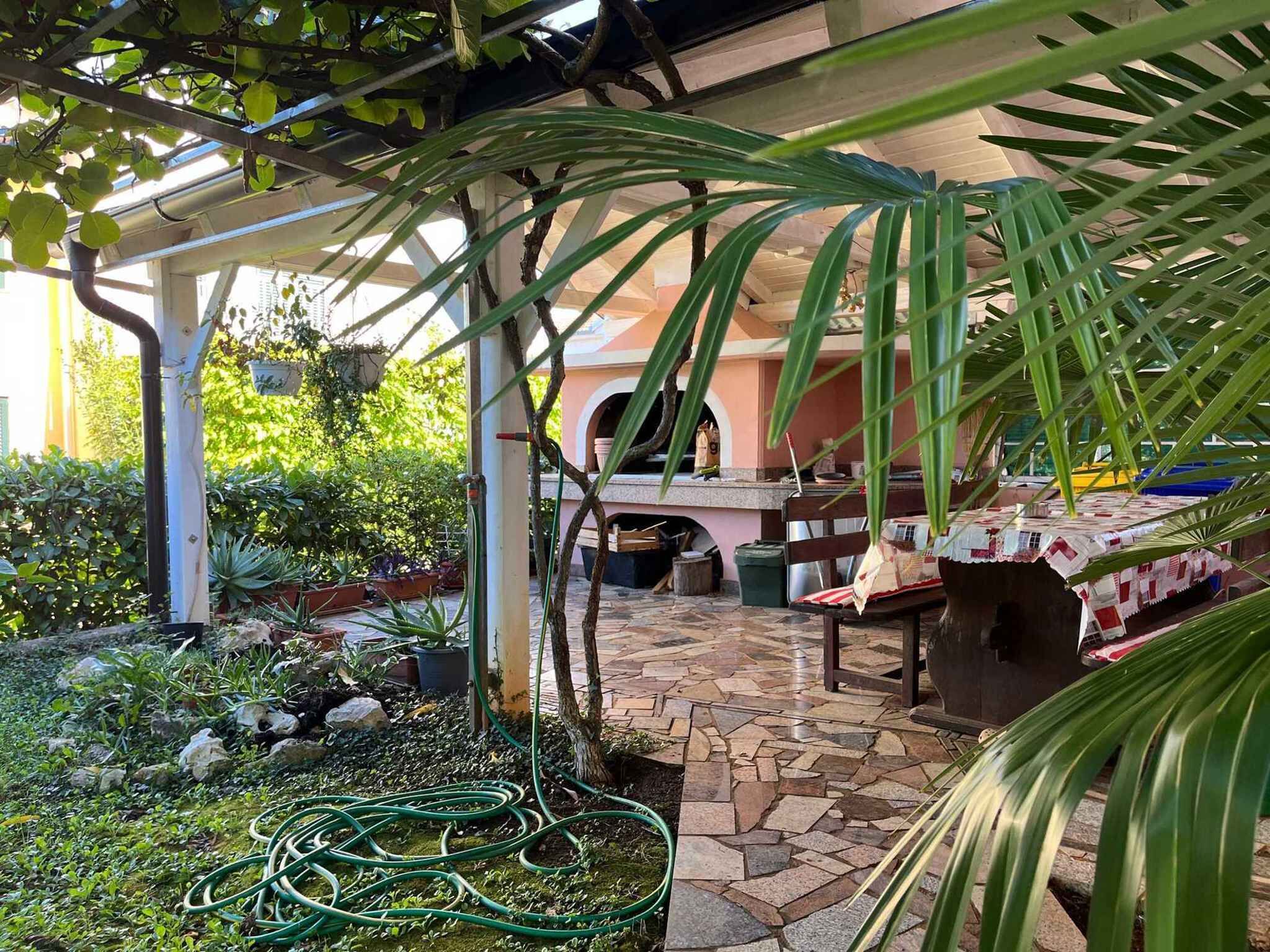 Un patio cubierto con suelo de piedra, una parrilla y diversas macetas con plantas.