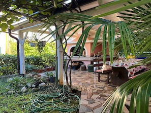 Un patio cubierto con suelo de piedra, una parrilla y diversas macetas con plantas.
