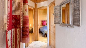 A narrow hallway with wooden walls and a wooden ceiling, leading to a bedroom with a bed and a pink pillow.