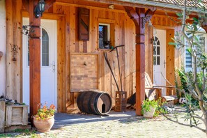 Una construcción de madera con chimenea de ladrillo, un barril de madera y una planta en maceta.