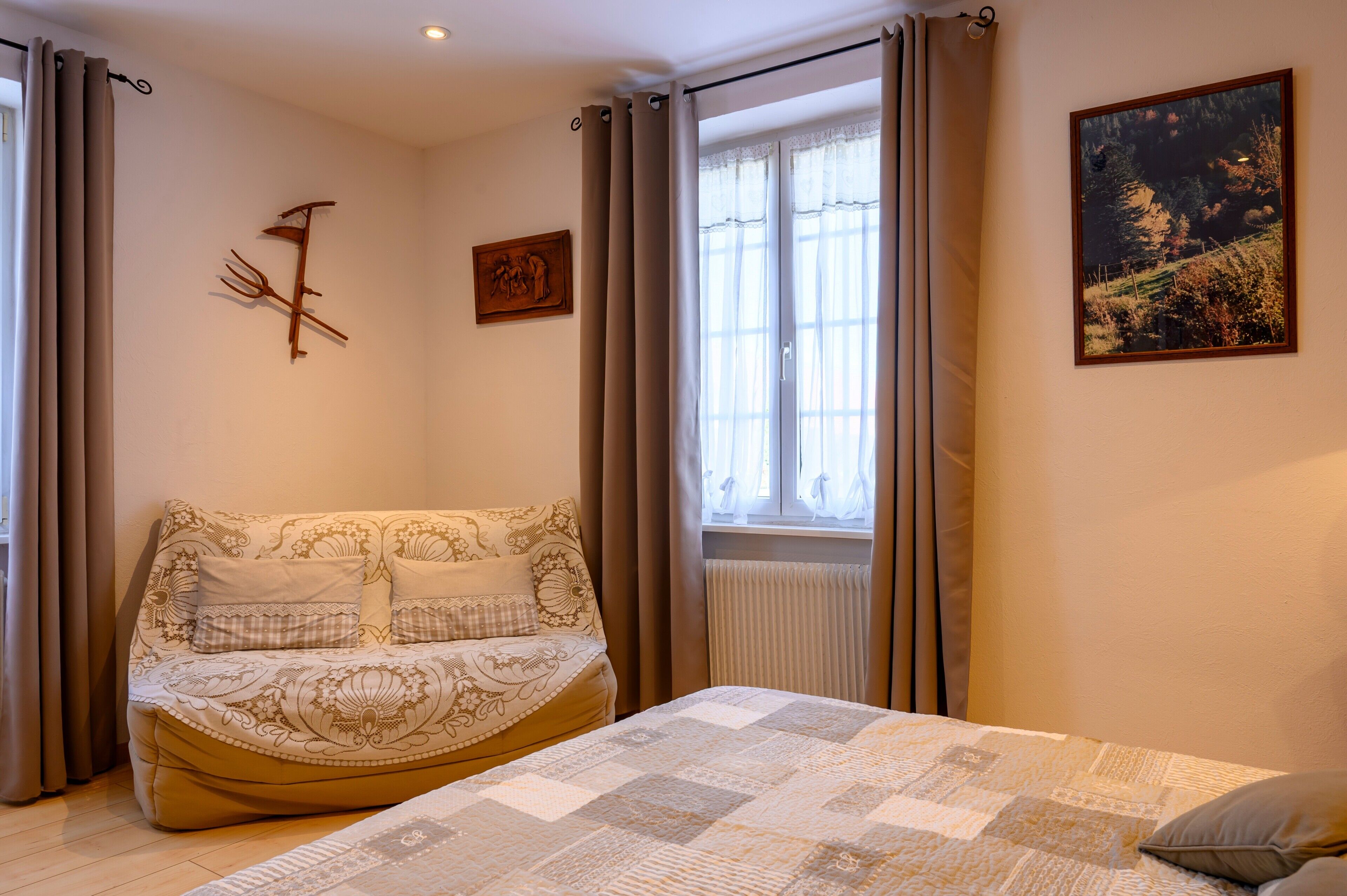 Um quarto com cama, janela com cortinas, um quadro na parede e um radiador.