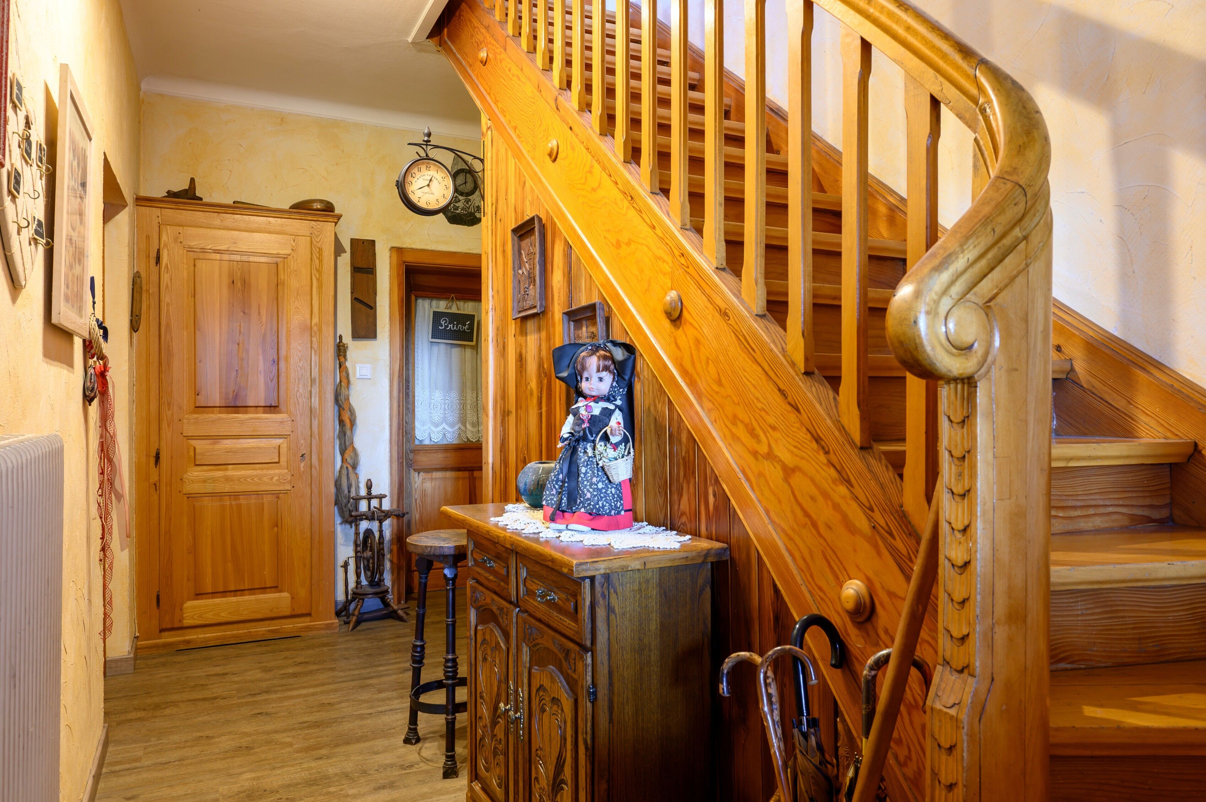 A wooden staircase with a clock, a wooden cabinet, and a small table with a doll.