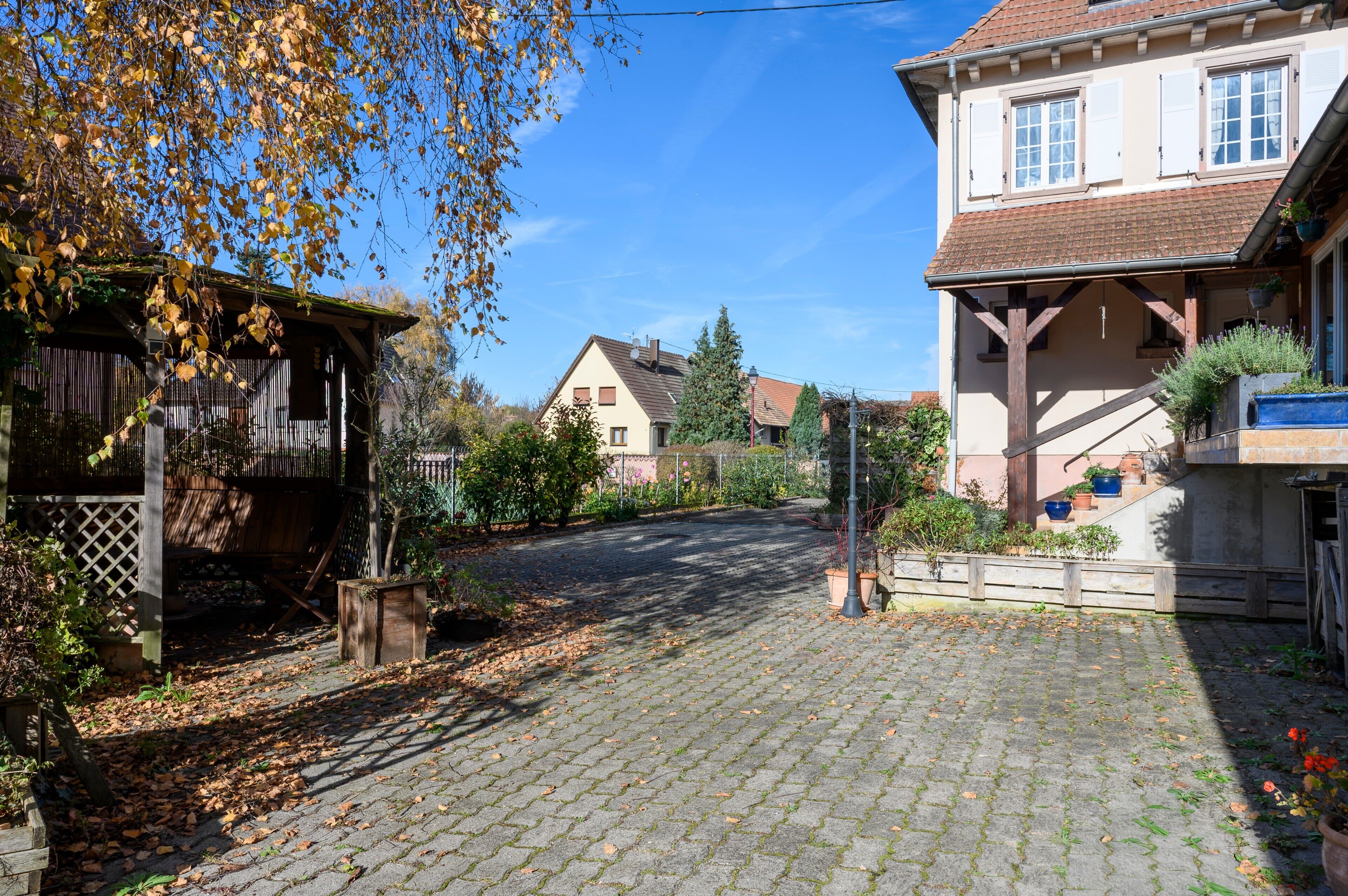 Eine gepflasterte Straße führt zu einem traditionellen Gebäude mit Holzzaun und Garten.