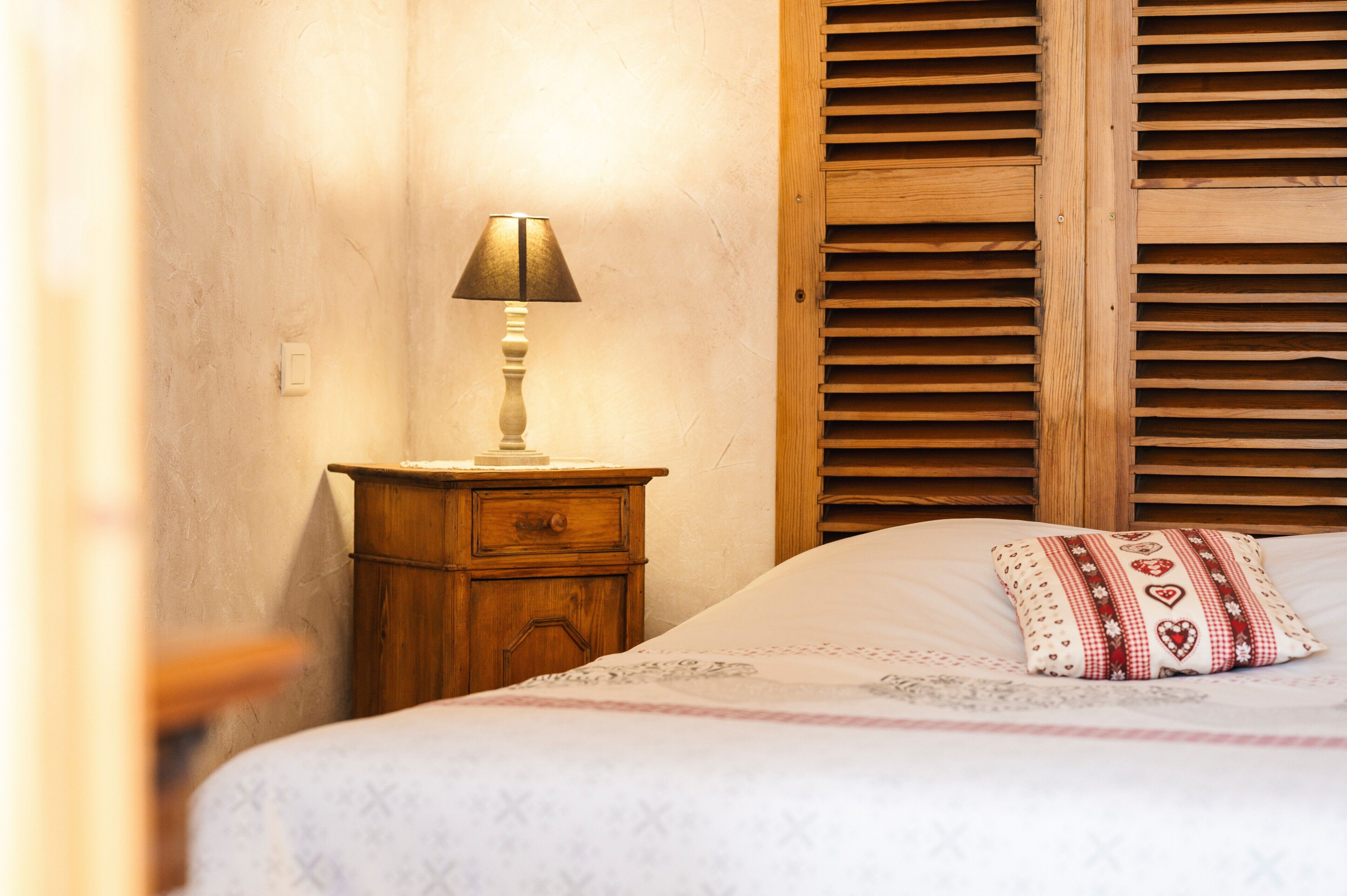 A bed with a patterned bedspread, a bedside lamp, a wooden nightstand, and a wooden headboard.