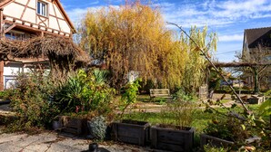 A garden with a bench, wooden planters, and a house with a sloped roof. - Guest Room and Table d'hôtes “À L'ancienne Boulangerie - Millet” (Elsenheim)