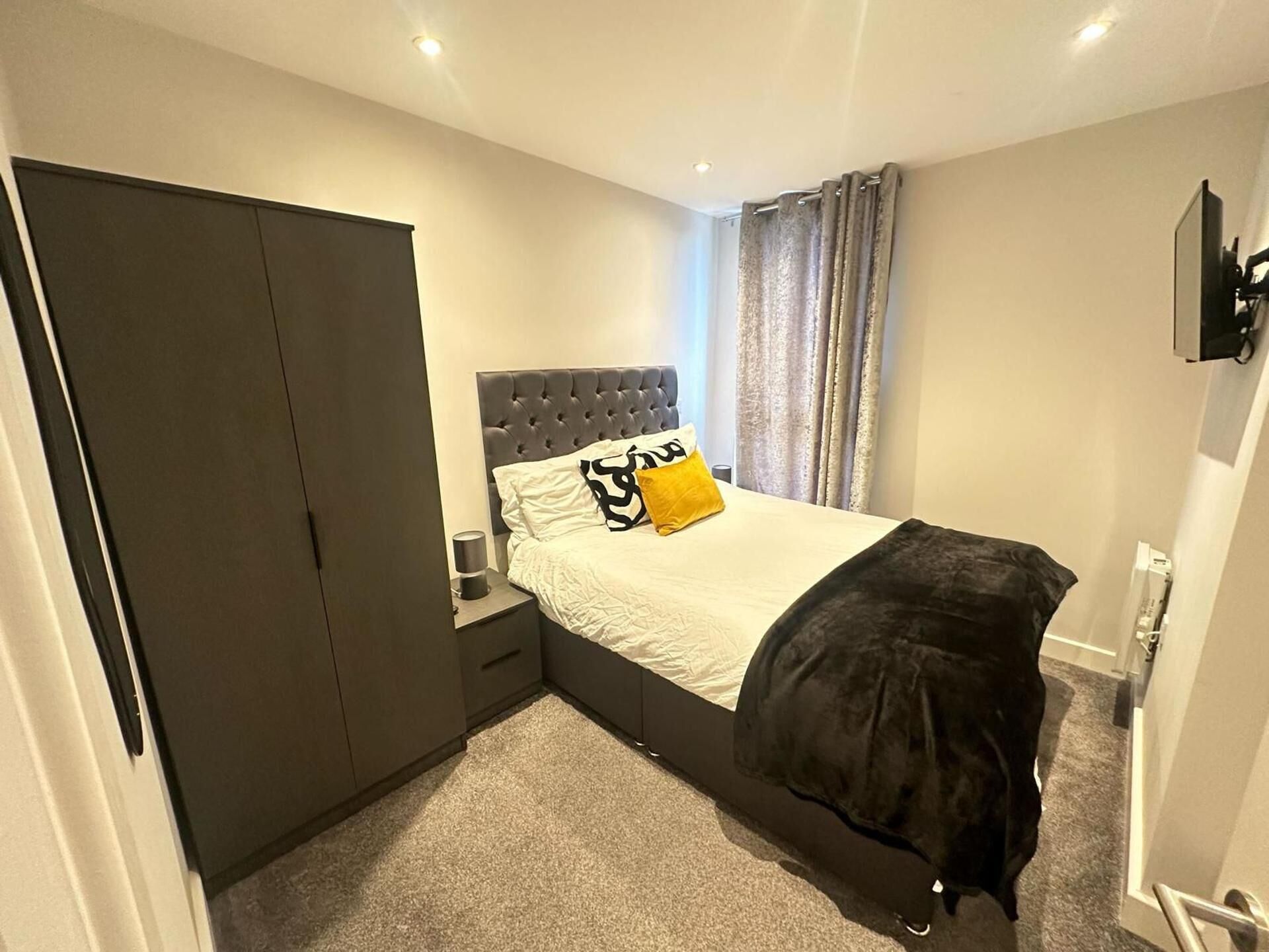 A bedroom with a bed, a wardrobe, a nightstand, and a television.