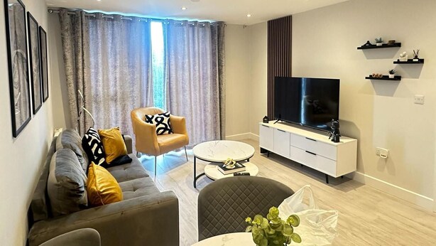 A modern living room with a sofa, armchair, coffee table, TV, and built-in shelves. - Salford City Retreat - 2 Bedroom Apartment (Salford)