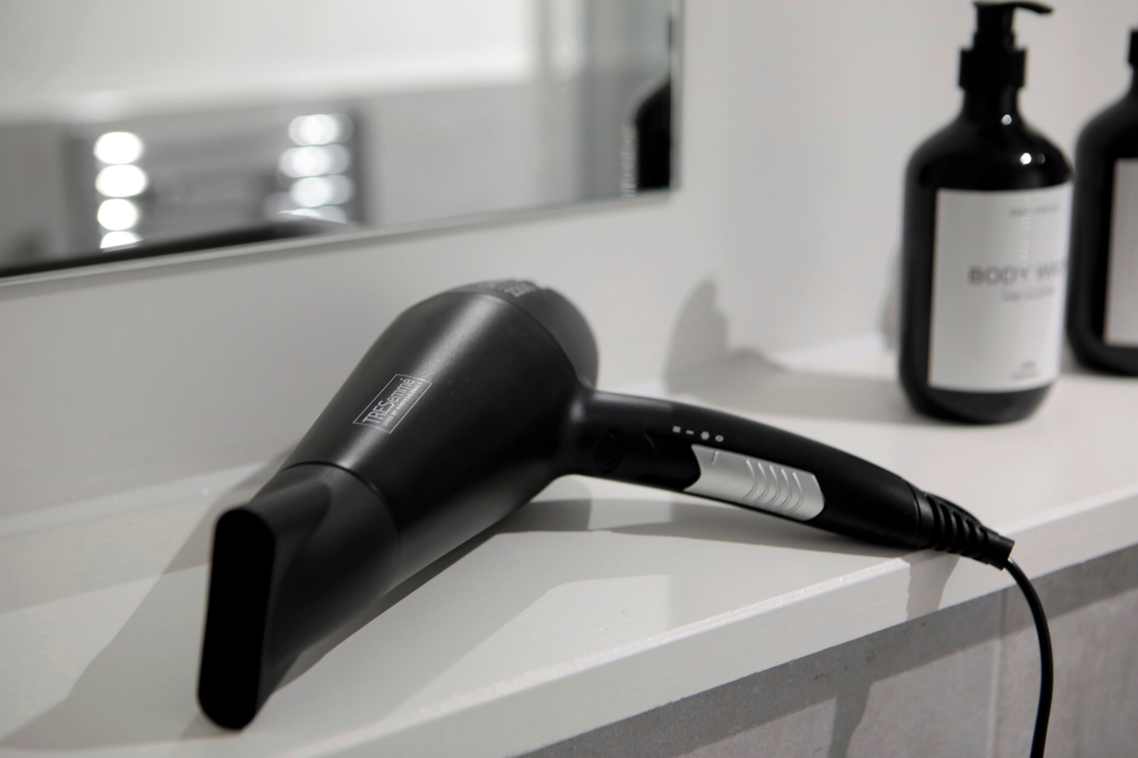 Een haardroger op een badkamermeubel, met een fles douchegel op de achtergrond.