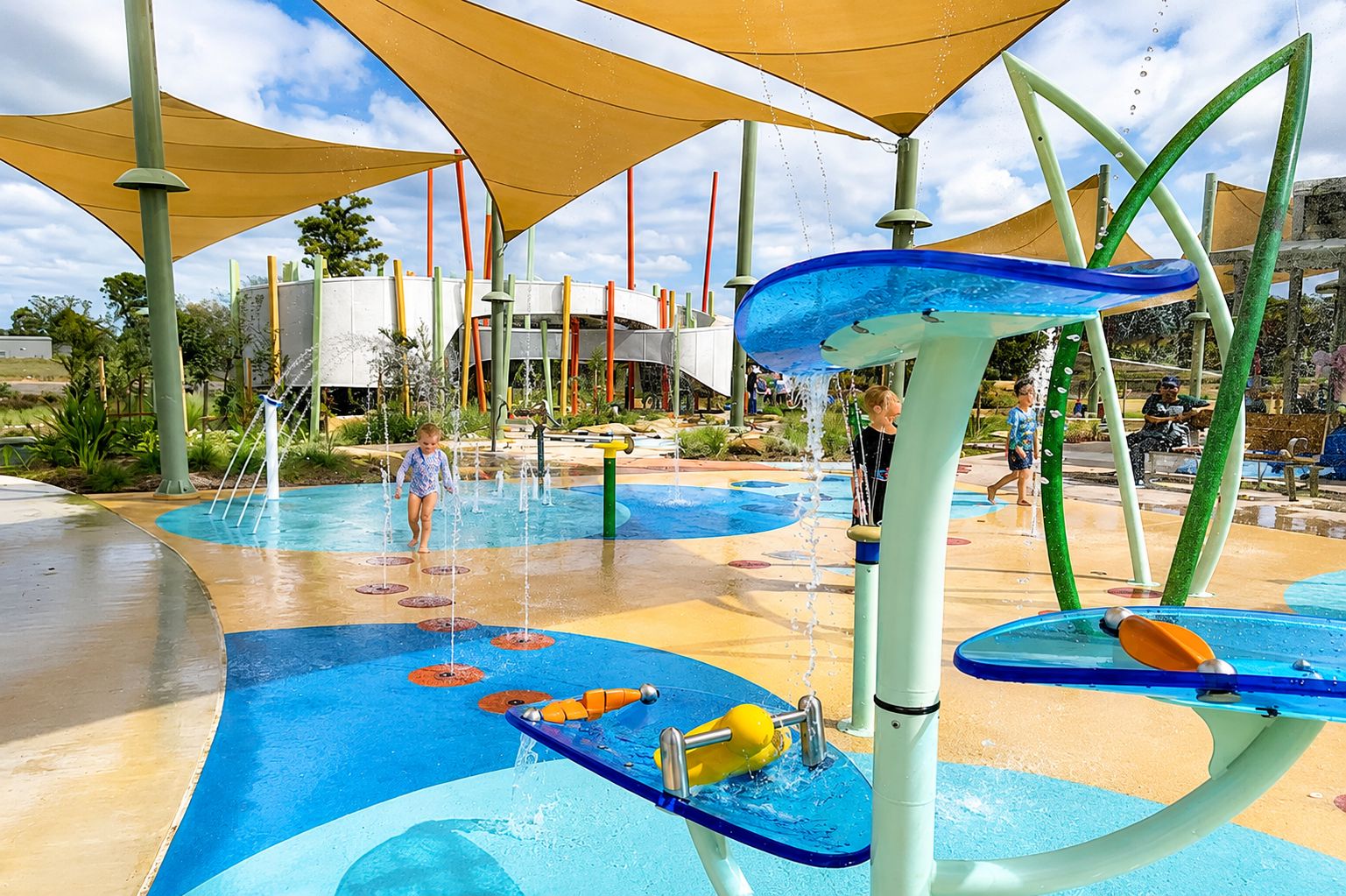Un'area giochi all'aperto con diverse fontane e un bambino che gioca.