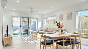 Ein großzügiges Wohnzimmer mit einer Couch, einem Couchtisch und einem Esstisch mit Stühlen. Eine Glastür führt zu einer Terrasse.