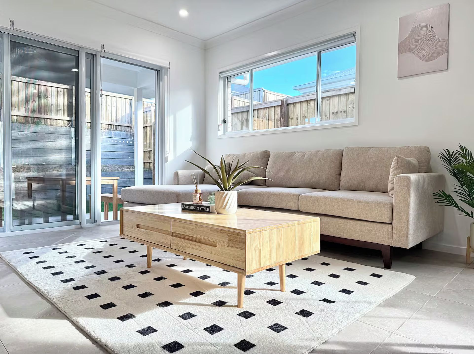 A modern living room with a beige sofa, a wooden coffee table, and a patterned rug.