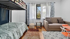 Ein Schlafzimmer mit Etagenbett, einer Schlafcouch, einem kleinen Tisch und einem Fenster mit Vorhängen.