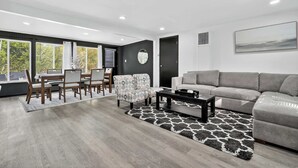 Ein modernes Wohnzimmer mit einem grauen Sofa, einem Esstisch mit Stühlen und einem gemusterten Teppich.