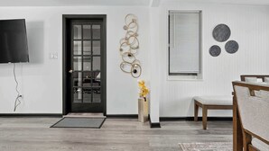 Ein modernes Interieur mit einer schwarzen Tür, einem wandmontierten Fernseher, einem Wanddekor und einem Essbereich mit Stuhl und Tisch.