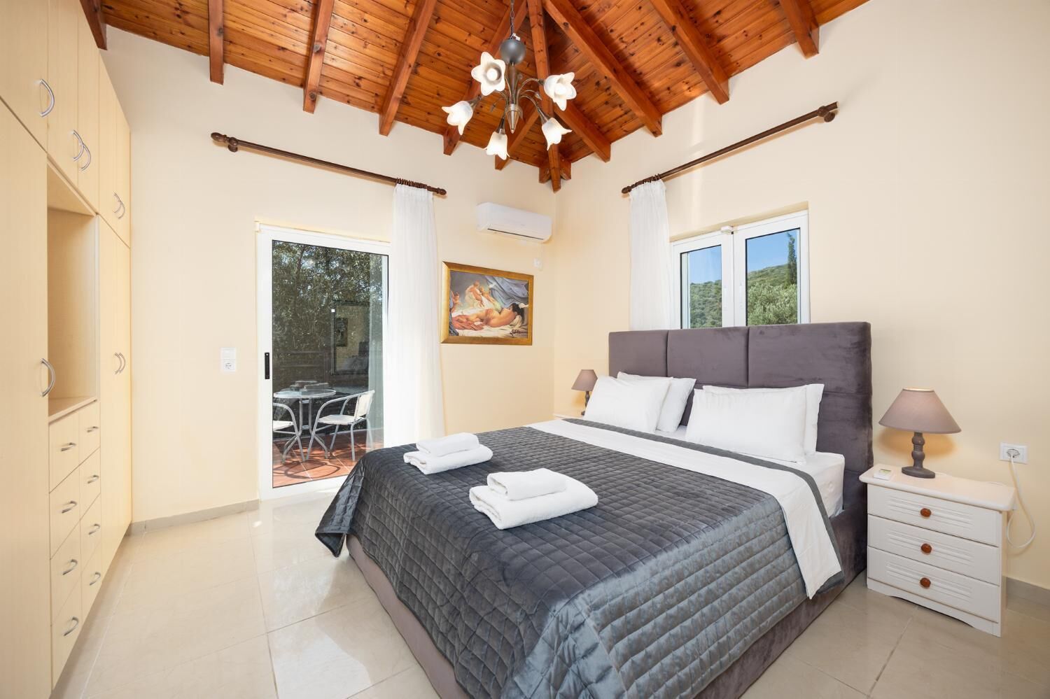 A bedroom with a large bed, a nightstand, a window, and a painting on the wall.