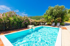 A swimming pool with a clear blue water surface, surrounded by lush greenery and pink flowering plants.