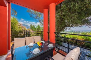 A balcony with a table set for two, surrounded by red walls and a view of greenery and hills. - Villa Aliona - Four Bedroom Villa, Sleeps 8 (Ionian Islands)