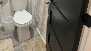 A bathroom with a white toilet, a beige rug, and a black door. - Canary Cottage in Beautiful Ailey, GA (Ailey)
