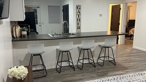 A modern kitchen with a bar area, white cabinetry, and a decorative sign. - Canary Cottage in Beautiful Ailey, GA (Ailey)