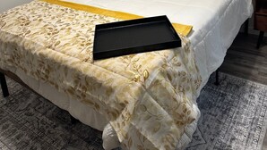 Un lit bien fait, recouvert d’une couvre-lit à motifs floraux, une lampe de chevet et un plateau posé sur le lit.