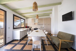Una cucina moderna con zona pranzo, mobili bianchi, una TV a schermo piatto e vista panoramica da una grande finestra.