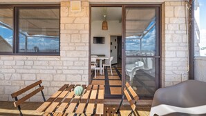 Een balkon met een houten tafel, een bank en een plastic stoel.