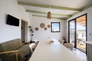 Una stanza con un tavolo lungo, sedie, un divano, una televisione a schermo piatto, piatti decorativi e una finestra.