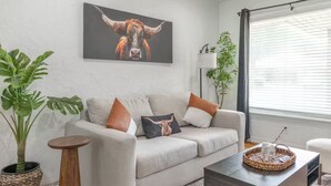 A living room with a sofa, a coffee table, and a painting of a bull. There is a plant and a lamp in the room. - Farm House - 1 min to Integris/State Fair/downtown (Oklahoma City)