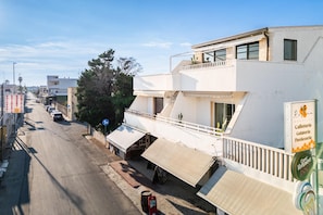 A street view with a white building featuring a balcony, a café sign, and a parked car.