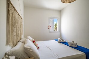 A hotel room with a bed, a macrame curtain, a window with a view, and a life preserver hanging on the wall.
