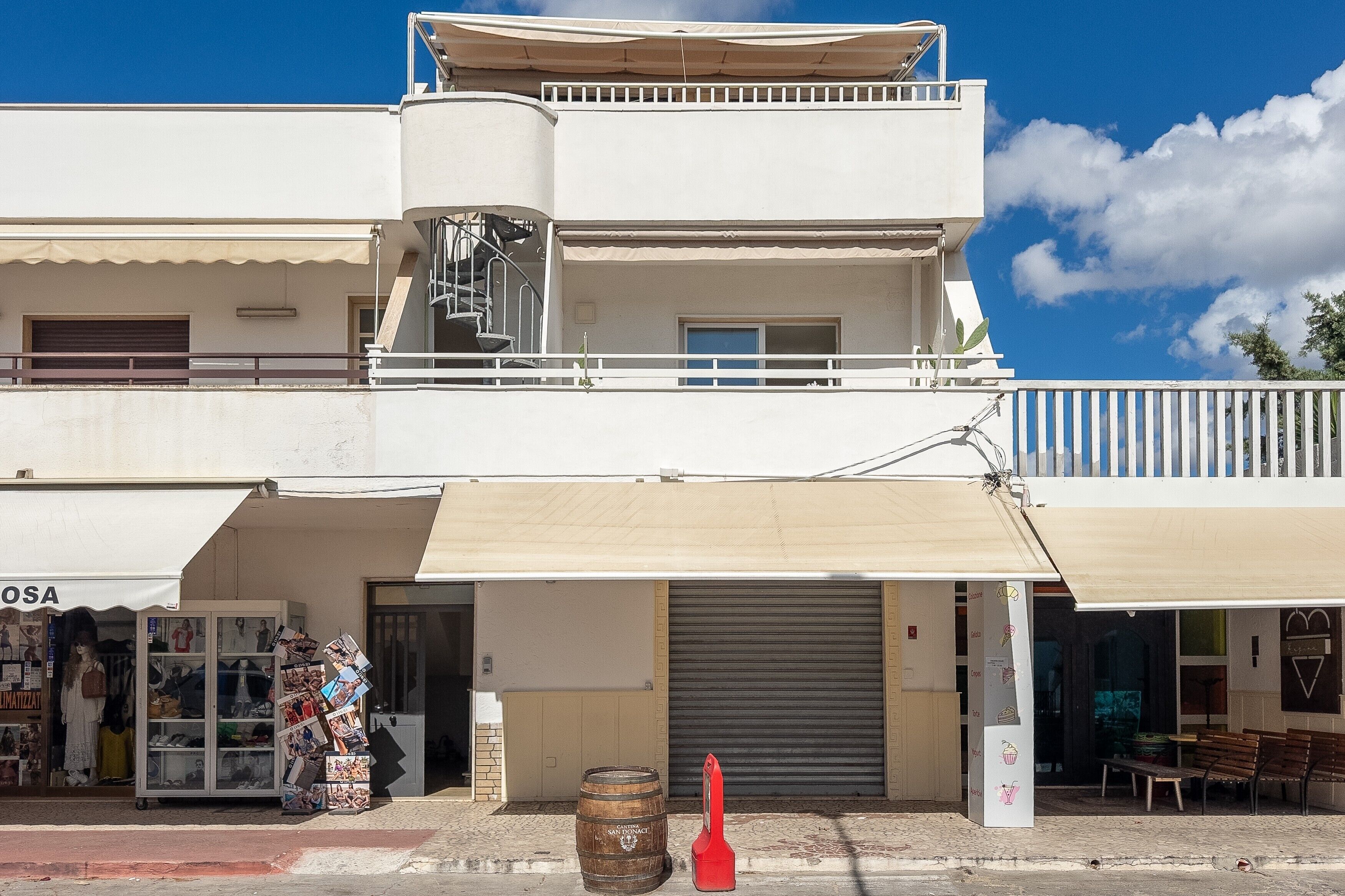 Un immeuble de deux étages, avec un commerce au rez-de-chaussée, un volet fermé et un balcon.