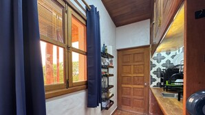 Un couloir étroit avec une porte en bois, une fenêtre avec des rideaux, une étagère contenant des ustensiles de cuisine et un sol carrelé.