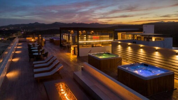 Eine Dachterrasse mit Sitzgelegenheiten im Freien, Whirlpools und Blick auf die Berge in der Abenddämmerung.