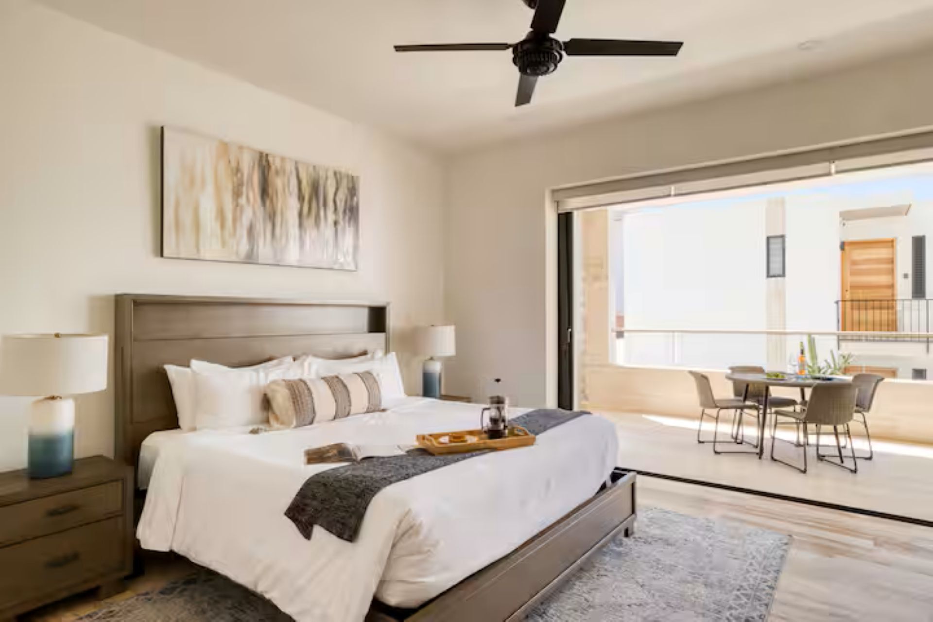 Une chambre dotée d’un grand lit, de lampes de chevet, d’un ventilateur de plafond et offrant une vue sur un balcon extérieur avec des chaises.