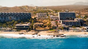 Ein Hotel an der Küste mit mehreren Gebäuden, einem Strand und einer Bergkulisse.